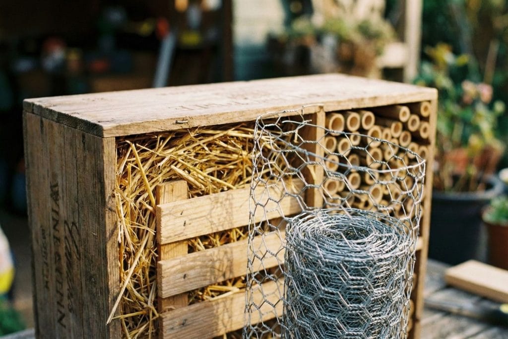 Installation du grillage à poule sur la façade de l'hôtel à insectes pour protéger la paille et les bambous des oiseaux.